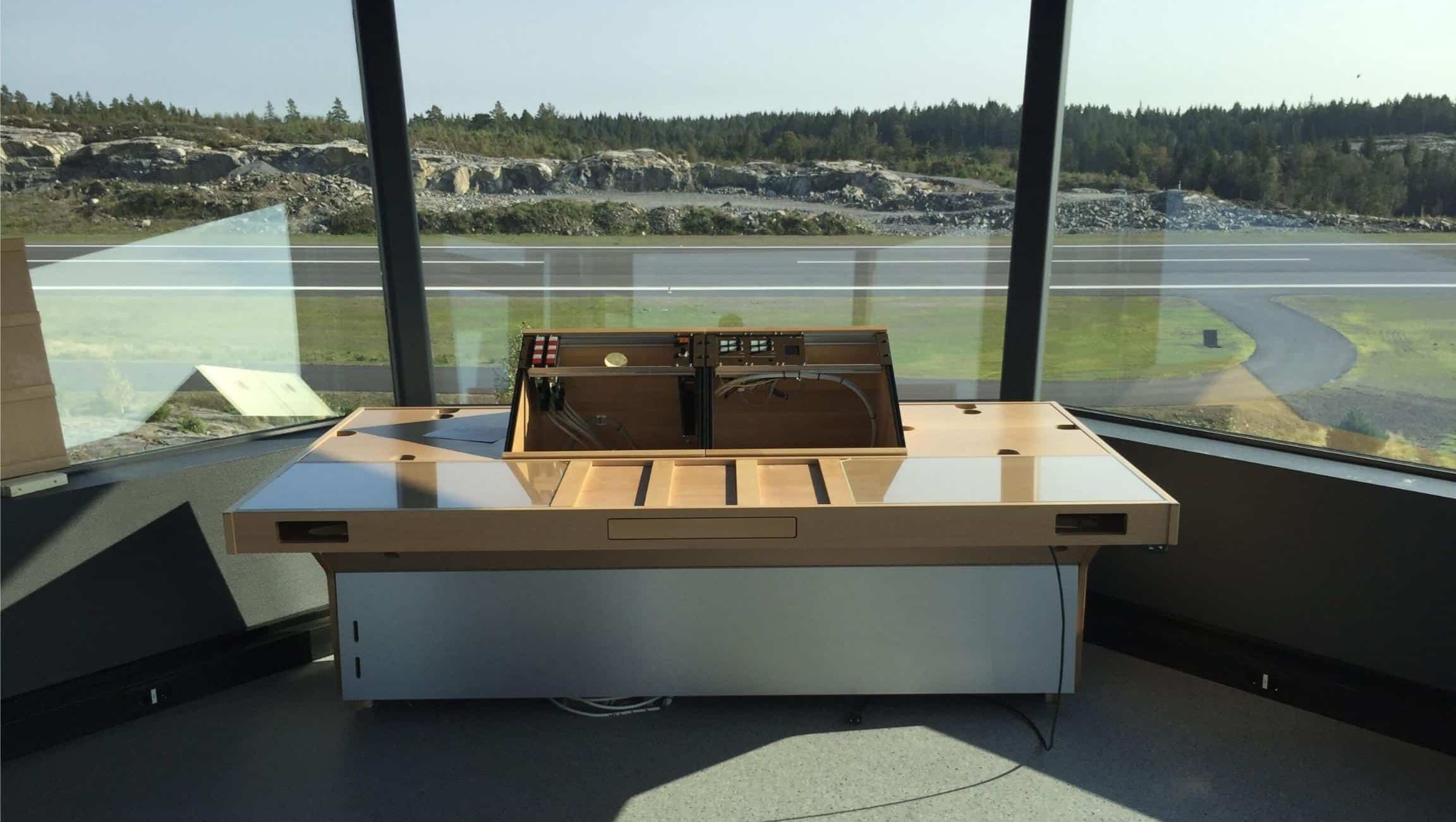 Kontrolltårn med arbeidsplass og utsikt over flystripe og natur.