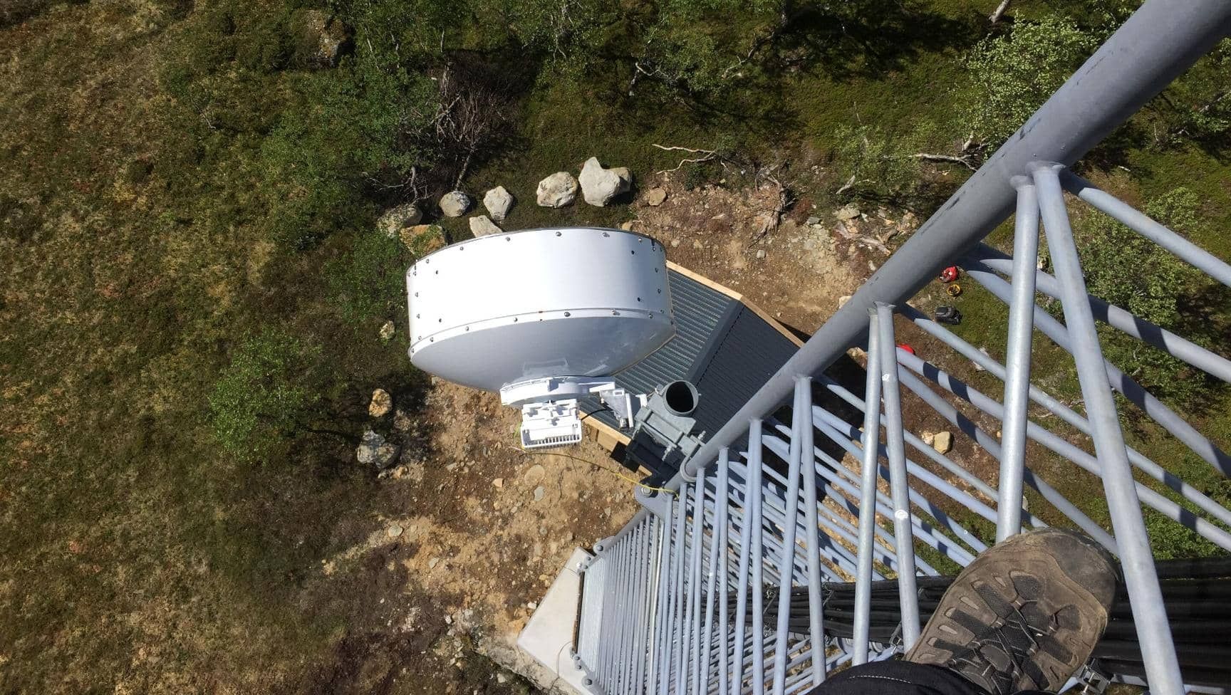 Utsikt ned fra radiotårn med fot på gittertrapp og antenne under.