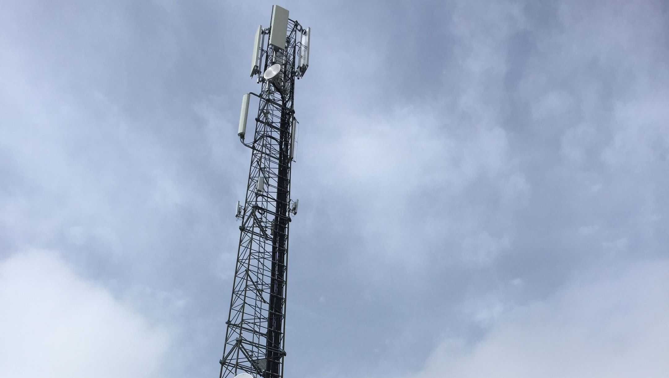 Radiomast med antenner og paraboler mot overskyet himmel.